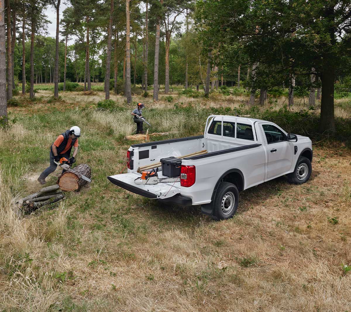 Ford Ranger in Weiß in der ¾-Heckansicht mit Werkzeug beladen parkt auf Wiese neben Waldarbeitern