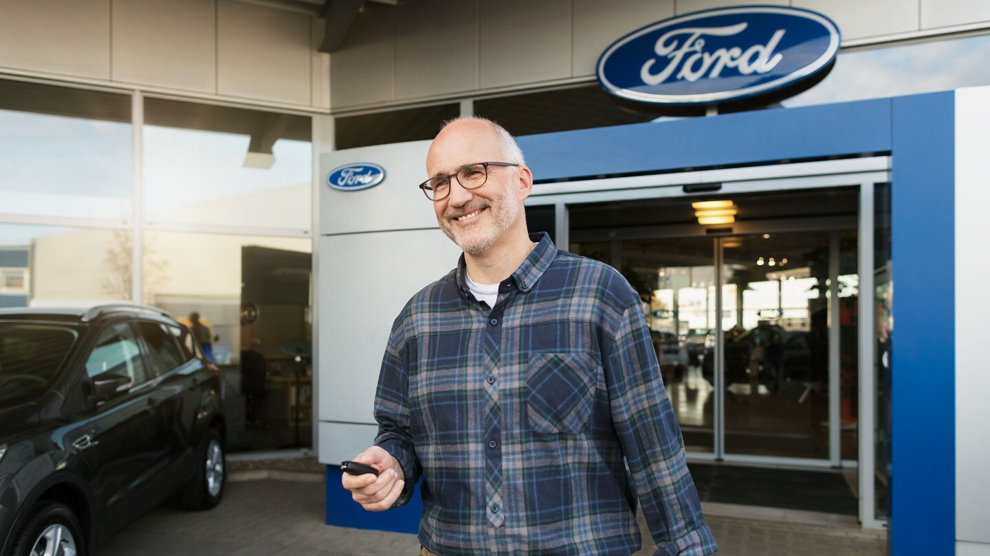 Man unlocking a car in front of Ford dealer