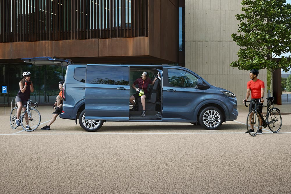 A blue Ford Tourneo Custom with open doors, parked kerbside. Cyclists prepare for a ride.