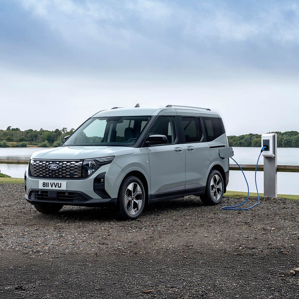 Ein grauer Ford E-Tourneo Courier lädt an einer Ladestation an einem See.