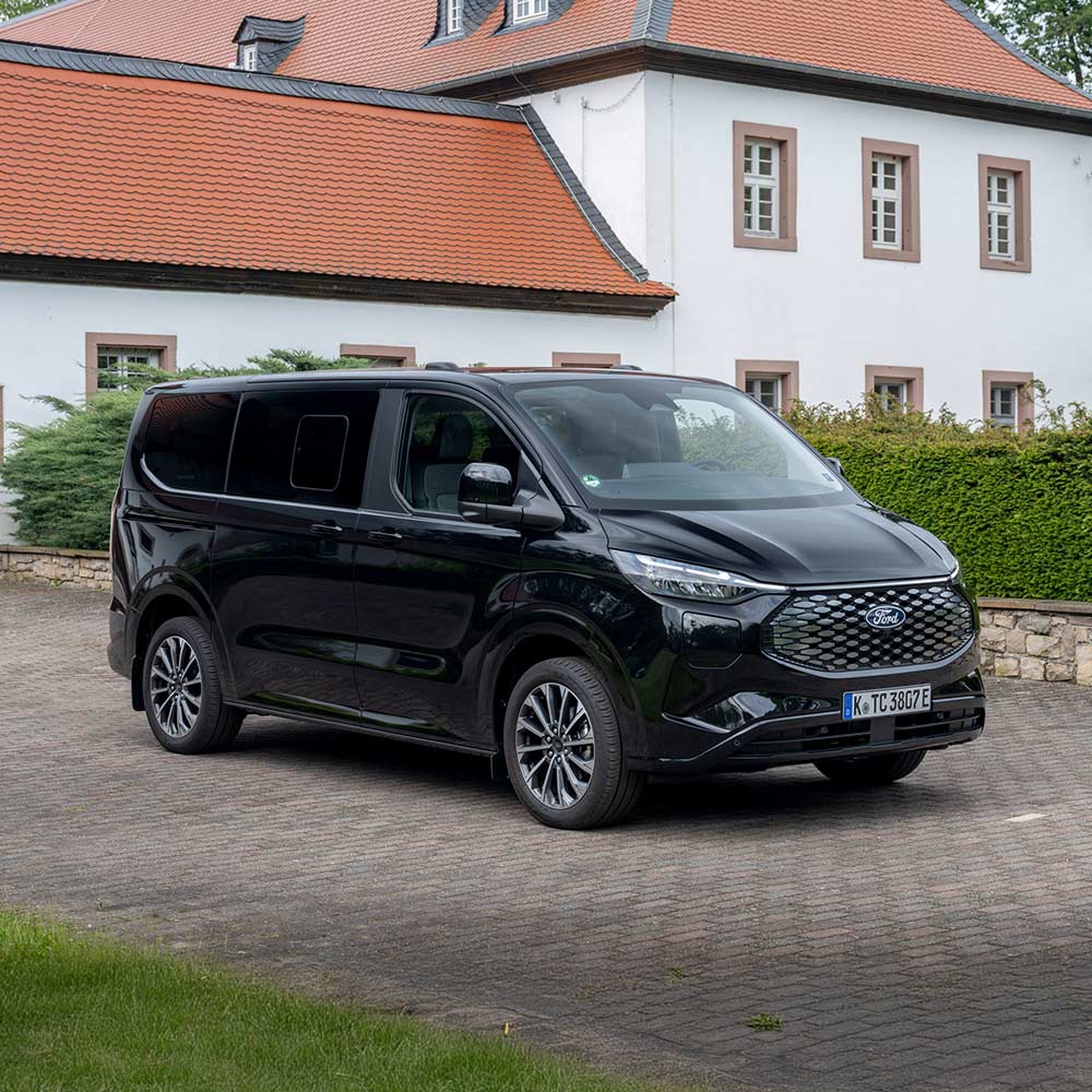 Ein schwarzer E-Tourneo Custom parkt vor einem Haus.