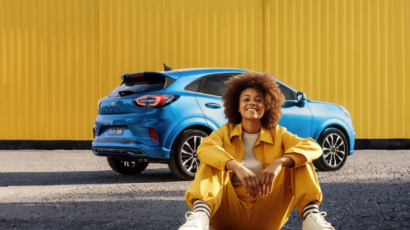 Frau lehnt auf der Motorhaube des Ford Puma Vivid Ruby Edition 