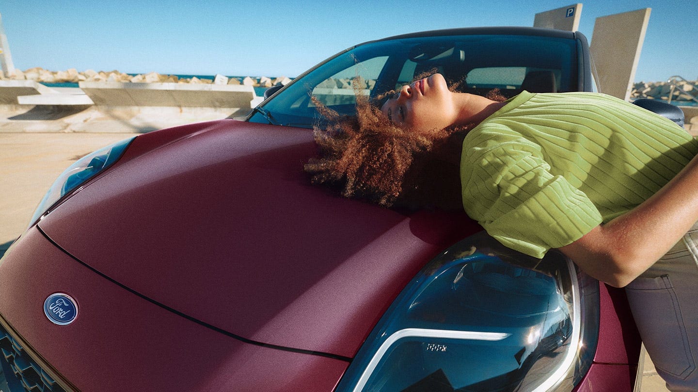 Frau lehnt auf der Motorhaube des Ford Puma Vivid Ruby Edition 