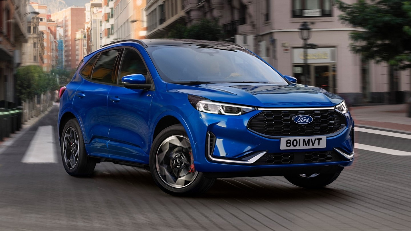 Ein blauer Ford Kuga Plug-in-Hybrid fährt auf einer Asphaltstraße in einer Stadt.