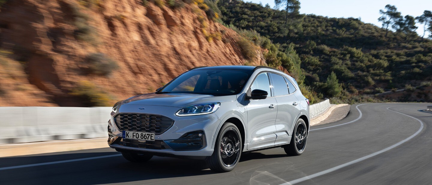 Ford Kuga ¾-Frontansicht in Graphite Edition, auf einer Straße vor Küstenlandschaft fahrend