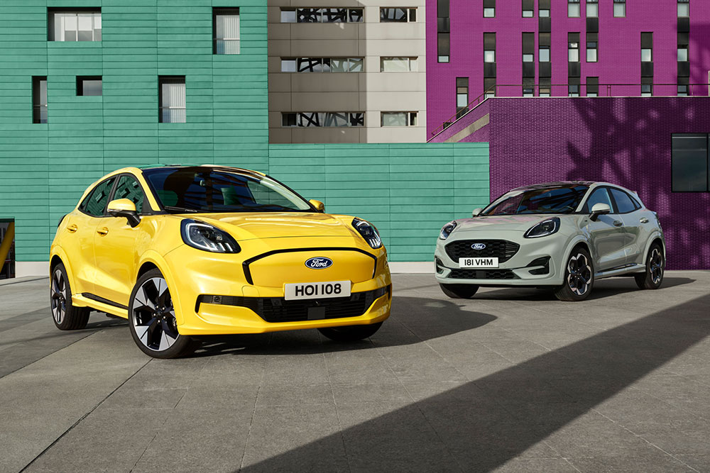 A yellow Puma Gen-E parked at a crossing on a sunny day. A man is walking past the electric car. 