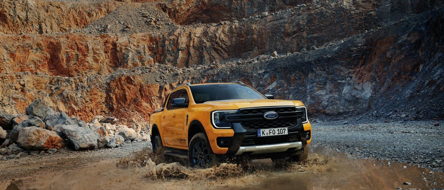 Ford Ranger-E ¾-Frontansicht in Orange, durch eine Pfütze innerhalb eines Steinbruchs fahrend