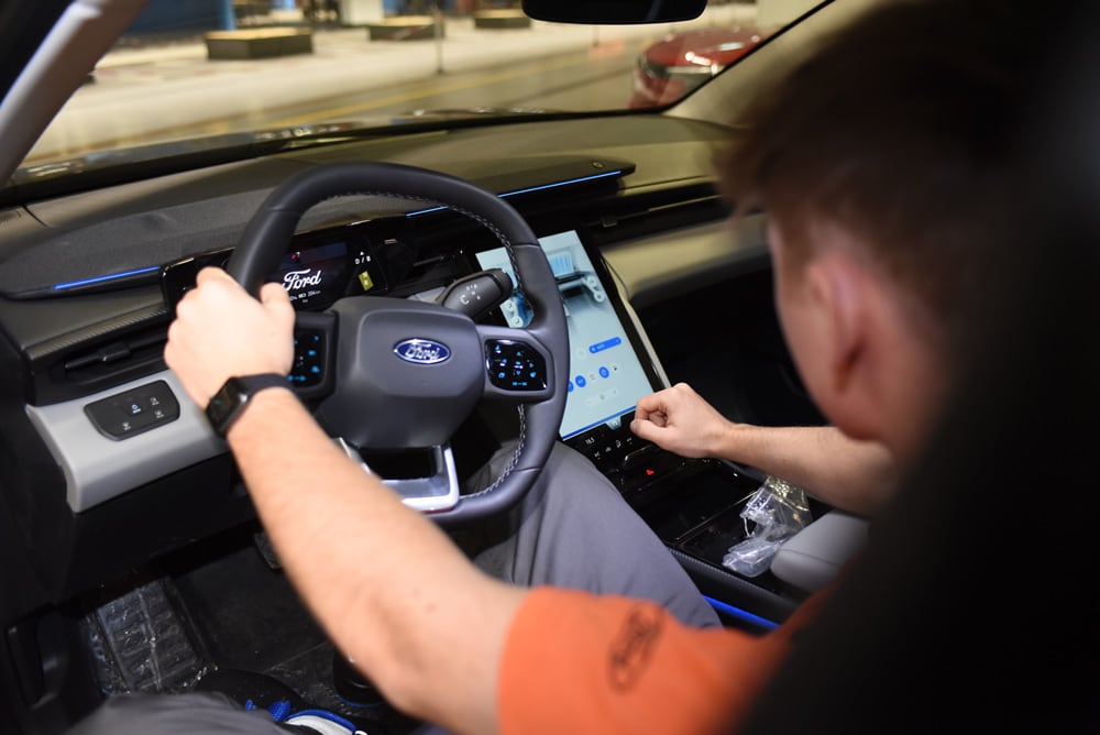 Eine Person hält das Lenkrad eines Ford, während eine andere den großen Touchscreen bedient.