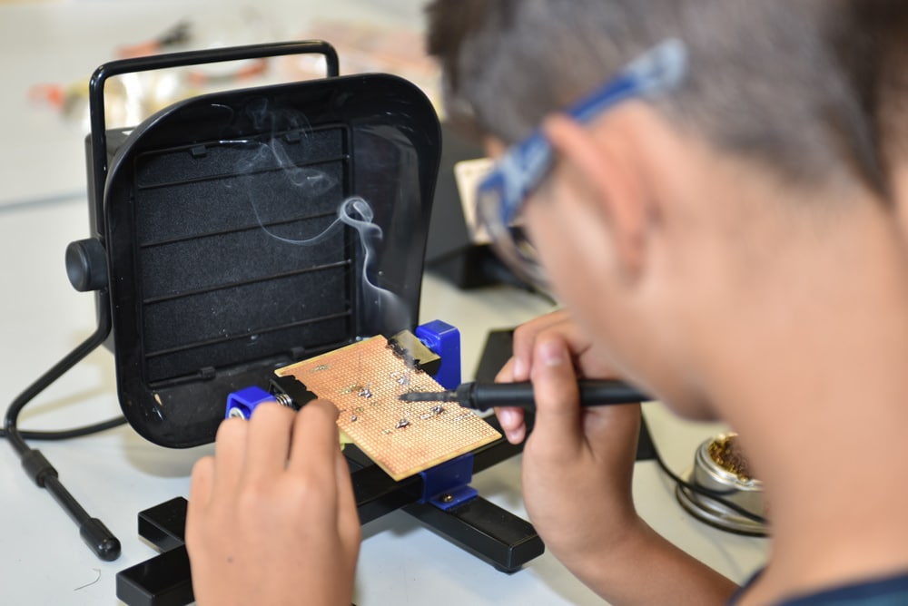 Eine Person lötet Bauteile auf eine Platine vor einem Lötrauchabsauger.