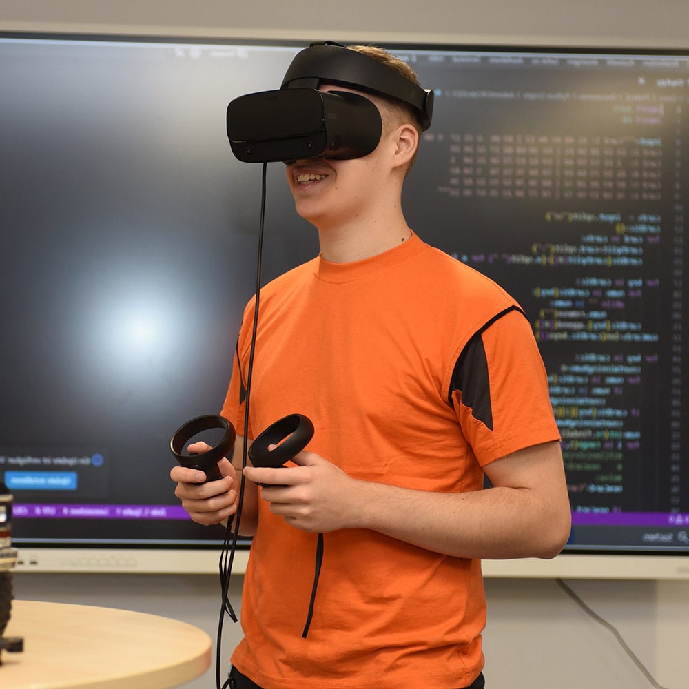 Eine Person trägt ein VR-Headset und hält Controller vor einer Anzeigetafel.