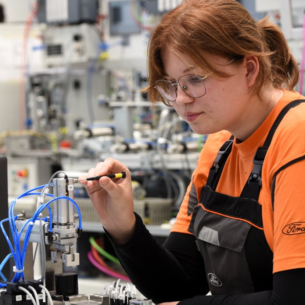 Eine Technikerin arbeitet mit einem Feinwerkzeug an elektronischen Bauteilen in einer Laborumgebung.
