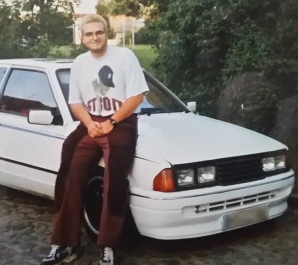 A man sitting on the car hood of a white Ford
