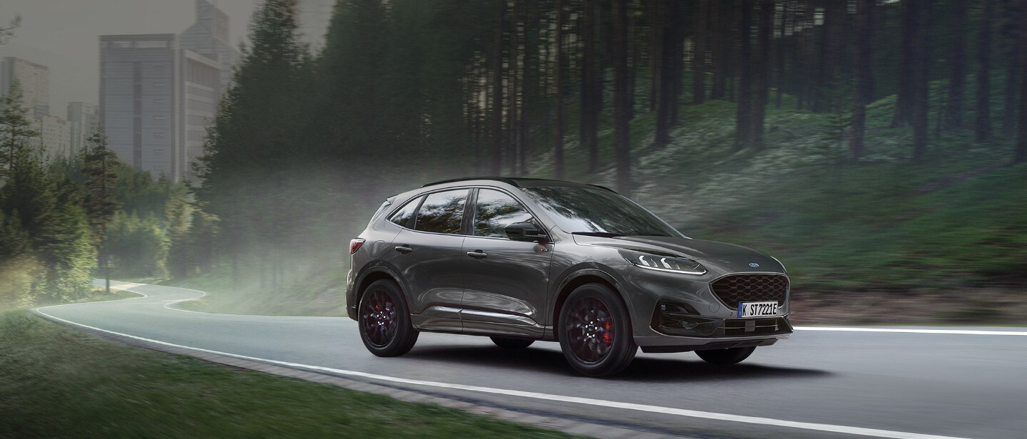 Ford Kuga ¾ Frontansicht in Rot auf einer Straße fahrend vor Küstenpanorama Ford Kuga ¾ Frontansicht in Rot auf einer Straße fahrend vor Küstenpanorama