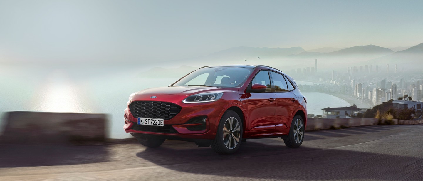 Ford Kuga ¾ Frontansicht in Rot auf einer Straße fahrend vor Küstenpanorama Ford Kuga ¾ Frontansicht in Rot auf einer Straße fahrend vor Küstenpanorama