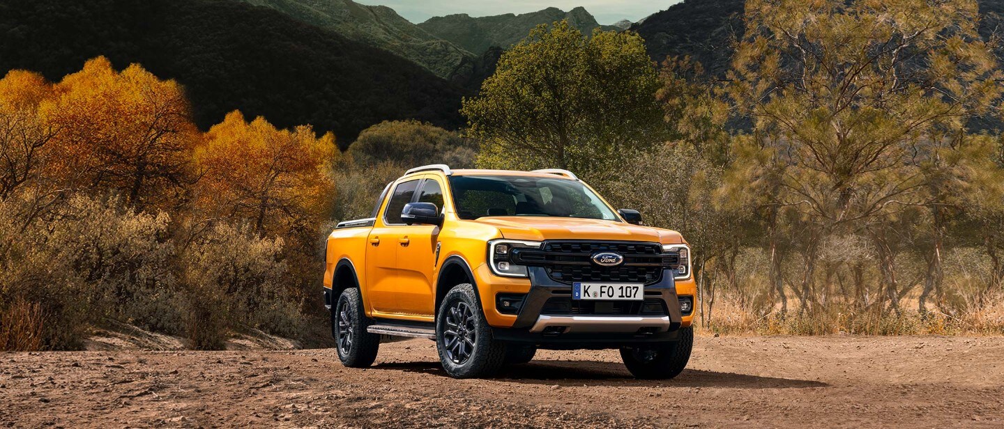 Ford Ranger ¾-Frontansicht in Orange, im Gelände stehend vor Bäumen und Bergen