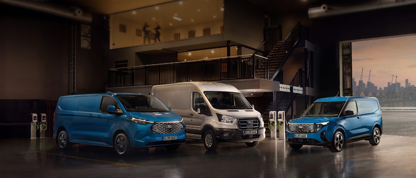 Drei elektrische Ford-Nutzfahrzeuge in einer Ladehalle mit Ladestationen im Hintergrund.