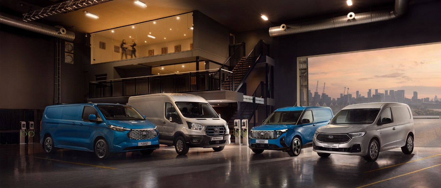 Vier Ford-Nutzfahrzeuge (E-Transit Custom, E-Transit, E-Transit Courier und Transit Connect PHEV) vor dem Hintergrund eines Innenraums mit Treppe und einem Fenster mit Blick auf eine Stadtlandschaft. Die Vans sind in verschiedenen Farben gehalten, darunter Blau und Grau.