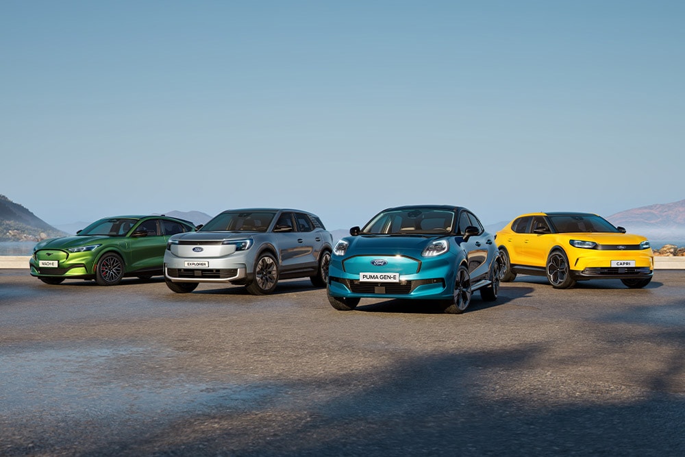 Vier Ford-Elektroautos (Mustang Mach-E, Explorer, Puma Gen-E, Capri) in einer Reihe an der Küste.