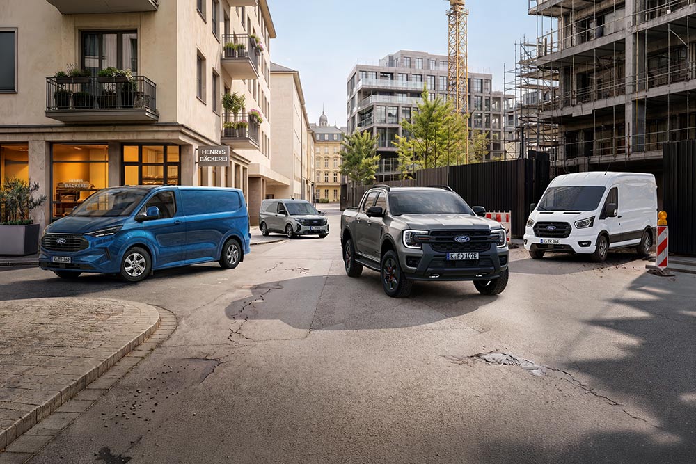  Ein grauer Tourneo Connect, ein grüner Kuga, ein silberner Capri und ein weißer Explorer stehen auf einer Stadtstraße.