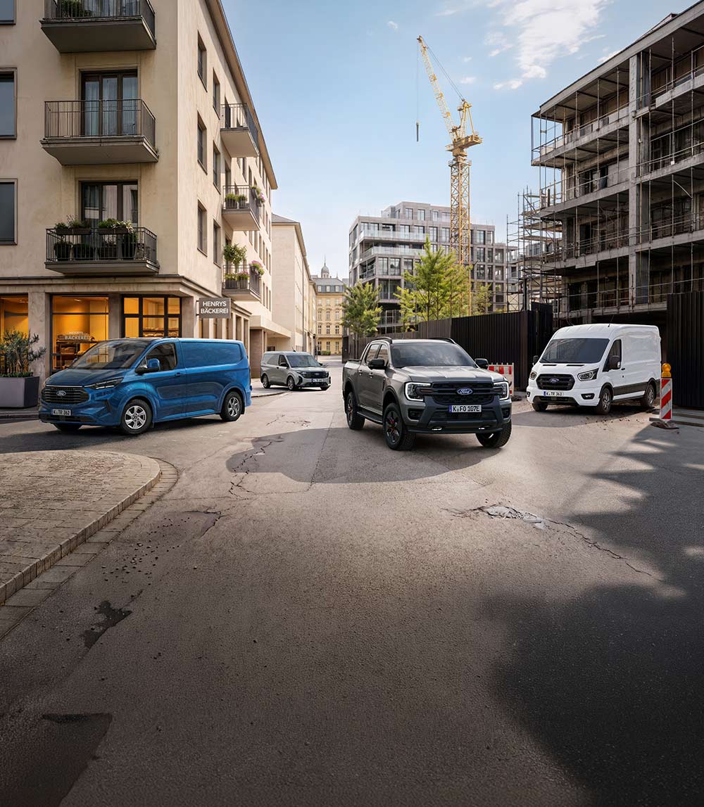 Vier Ford Nutzfahrzeuge, darunter ein grauer Ranger Pickup und blaue sowie weiße Transit Transporter, stehen auf einer Stadtstraße.