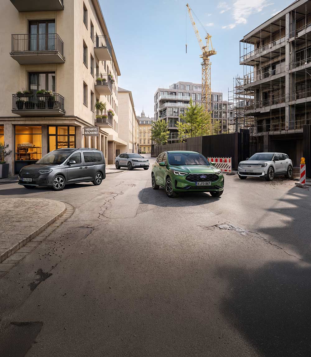  Vier Ford Nutzfahrzeuge, darunter ein grauer Ranger Pickup und blaue sowie weiße Transit Transporter, stehen auf einer Stadtstraße.