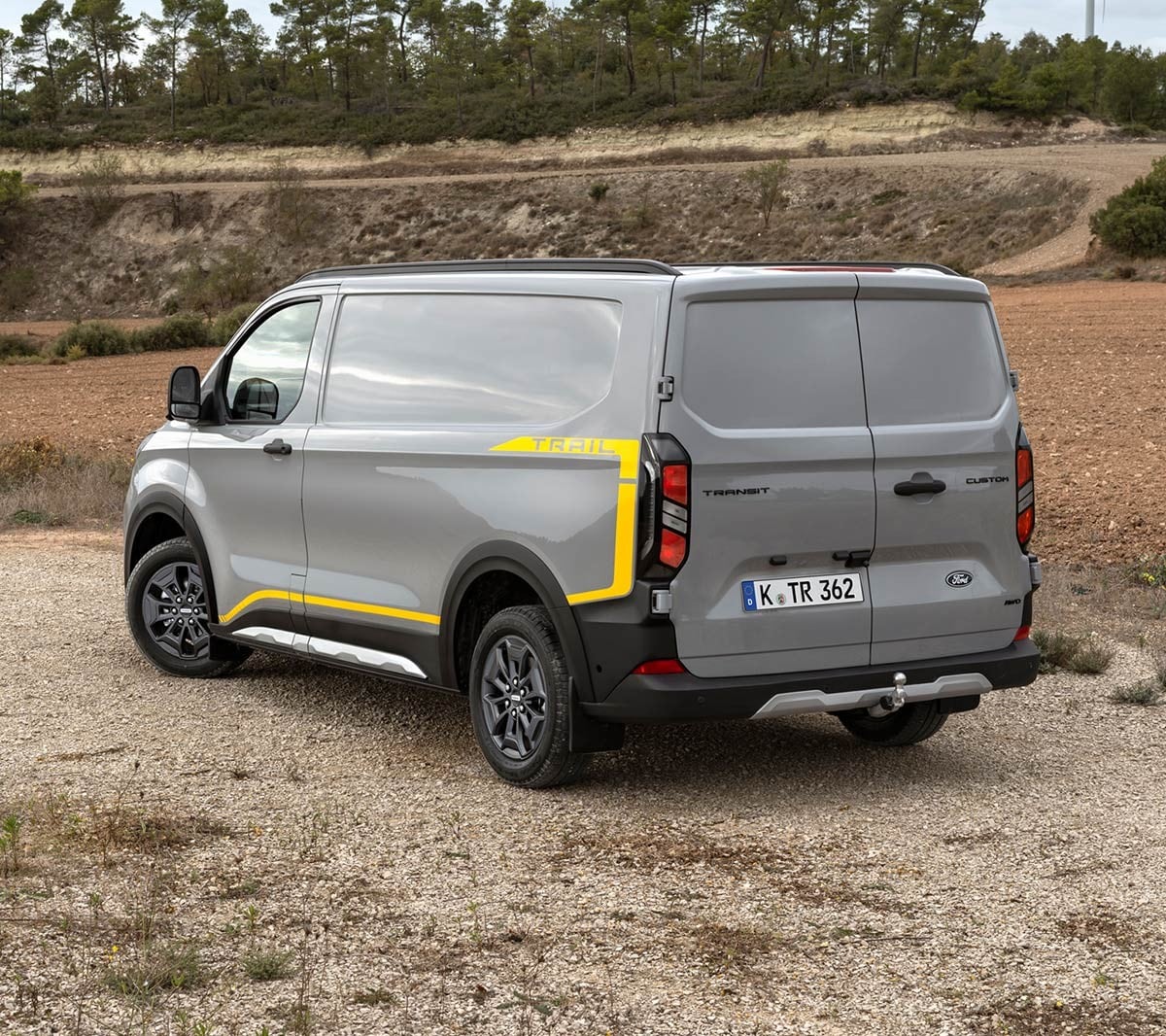 Ford Transit Custom in Grau in der ¾-Heckansicht parkt auf unbefestigtem Untergrund