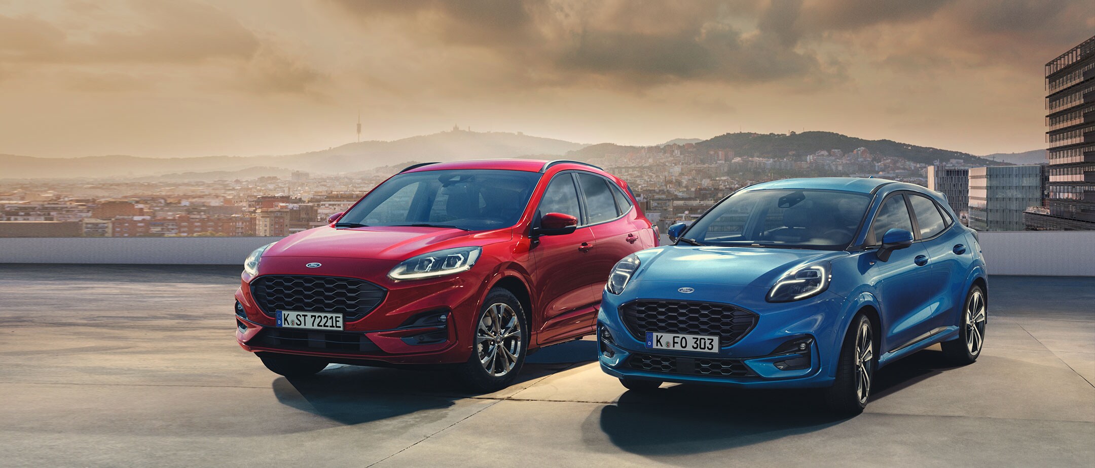 Ford Kuga in Rot, ¾ Frontansicht und Ford Puma in Blau, ¾ Frontansicht auf einem Parkdeck stehend