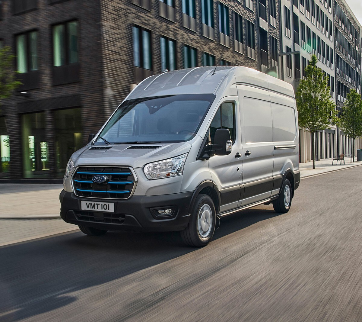 Ford E-Transit in Silber in der 3/4 Frontansicht durch die Stadt fahrend