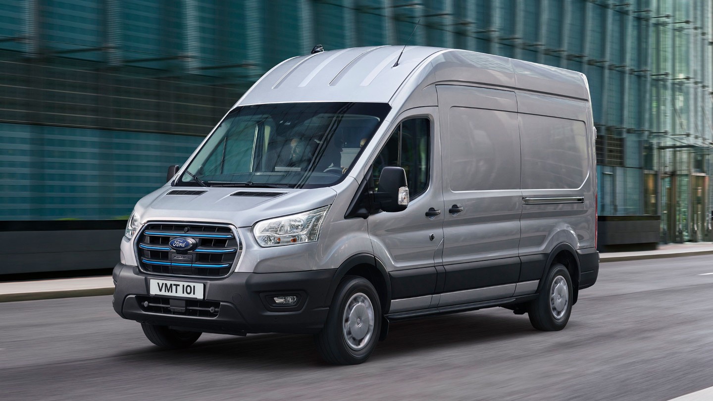 Ford E-Transit in Silber in der ¾-Frontansicht durch eine Stadt fahrend