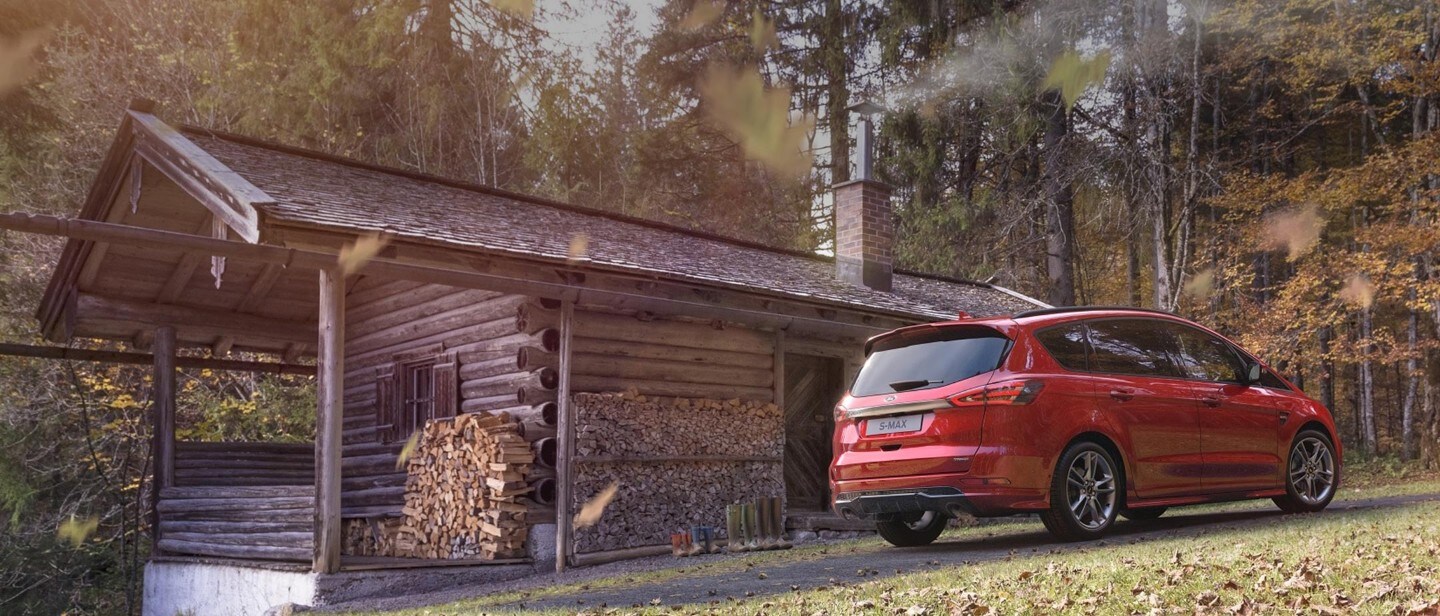 Ford S-MAX in Rot ¾-Heckansicht stehend vor Holzhütte im Wald
