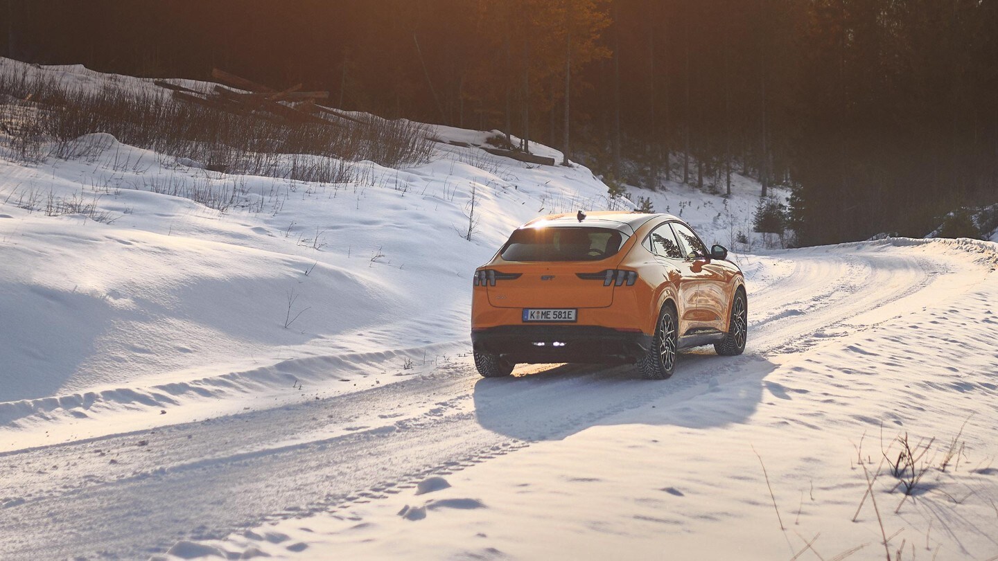 Ford Mustang Mach-E in Orange fahrend auf Straße im Schnee in Berglandschaft