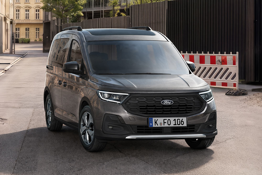  Ein dunkelgrauer Ford Tourneo Connect steht auf einer Straße, von vorne schräg gesehen, mit Absperrungen im Hintergrund.