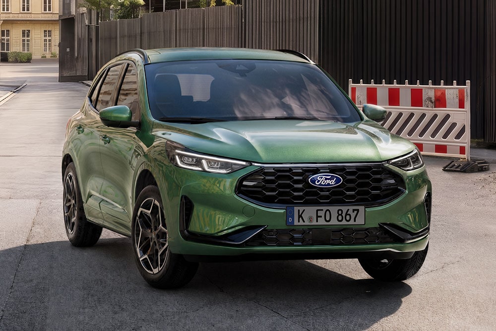  Ein grüner Ford Kuga SUV steht auf einer Straße, von vorne schräg gesehen, mit Absperrungen im Hintergrund.
