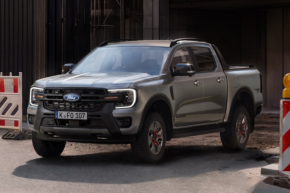 Ein grauer Ford Ranger Pick-up steht auf einer Straße, von vorne schräg gesehen, mit Absperrungen im Hintergrund. 