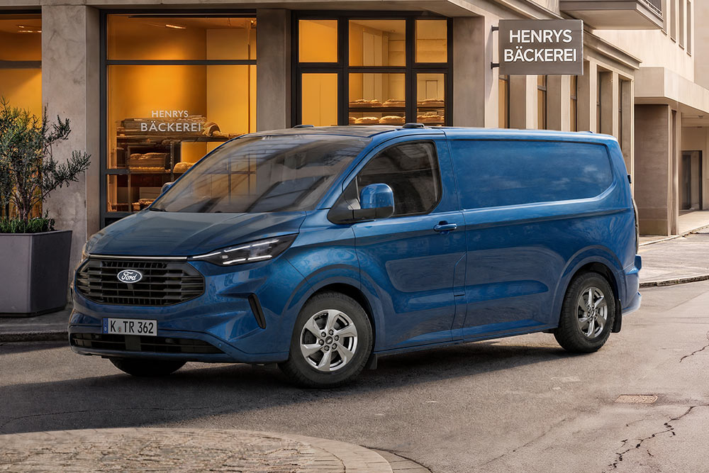  Ein blauer Ford Transit Kastenwagen steht auf einer Straße vor einer Bäckerei.