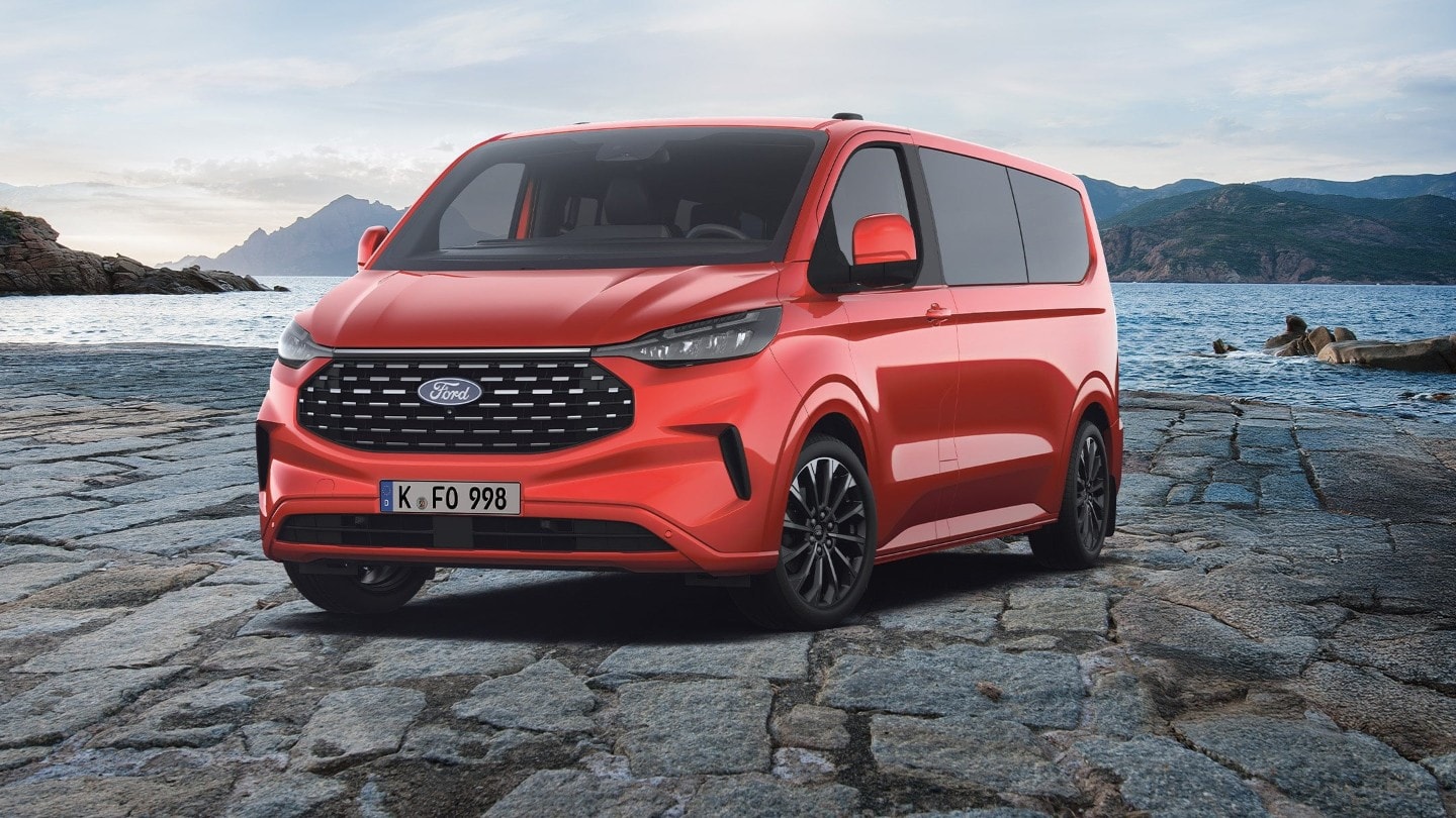 Zu sehen ist ein roter Ford Tourneo Custom mit Bergpanorama und Wasser im Hintergrund.