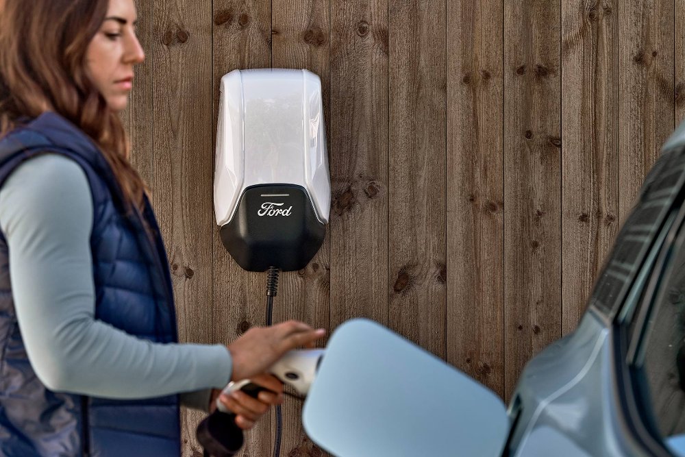 Eine Frau schließt den neuen Ford Explorer über ein Ladekabel  an die Ford Wallbox an