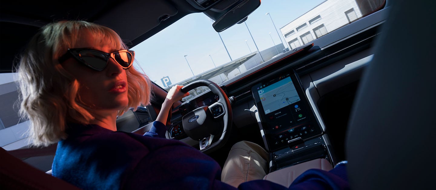 Nahaufnahme, die eine Frau auf dem Fahrersitz des elektrischen Ford Capri und auch den großen 14,6-Zoll-SYNC-Move-Touchscreen zeigt.