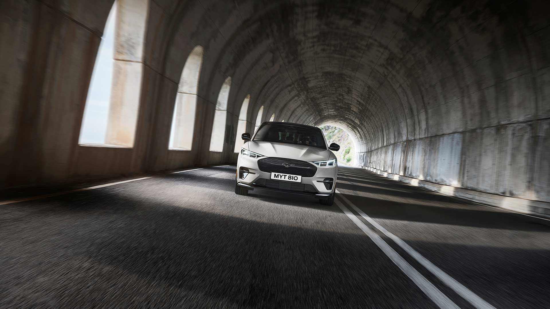 Ein silberfarbenes Ford Mustang Mach-E Elektrofahrzeug fährt durch einen Tunnel. 