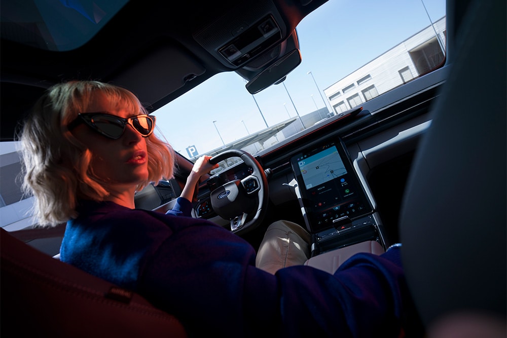 Nahaufnahme, die eine Frau auf dem Fahrersitz des elektrischen Ford Capri und auch den großen 14,6-Zoll-SYNC-Move-Touchscreen zeigt.