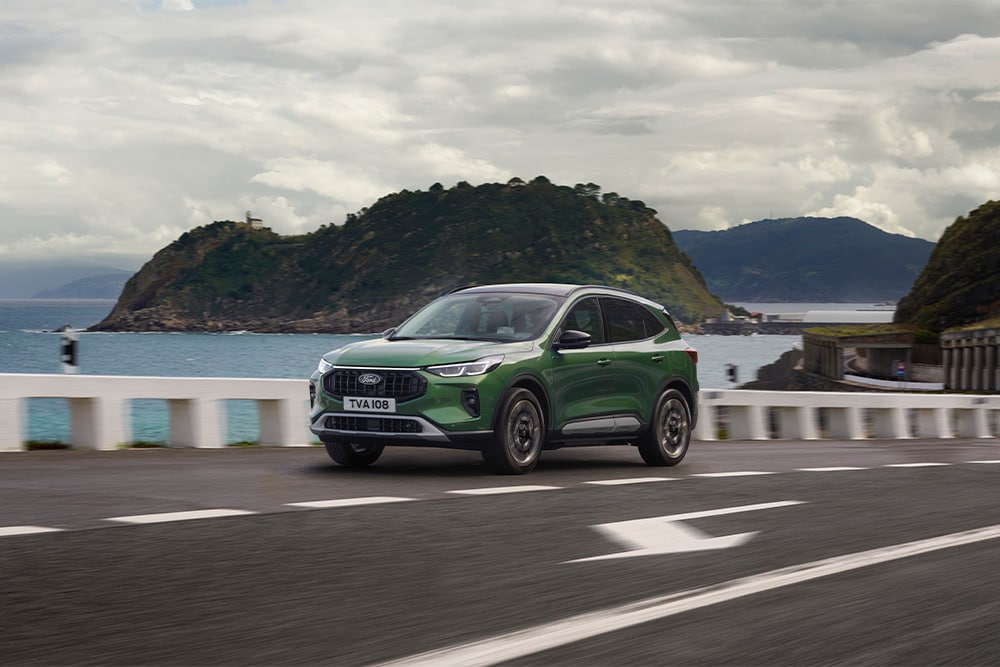 Ein grünes Ford Kuga Hybrid-Fahrzeug fährt auf einer Panoramastraße. 