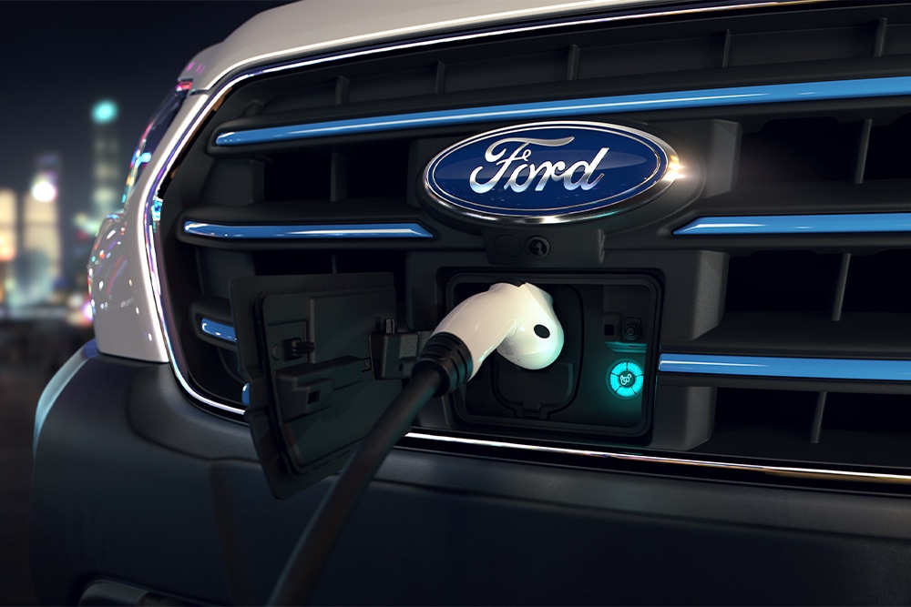 Nahaufnahme eines Ford E-Transit  und des blauen ovalen Ford-Schriftzugs auf dem Kühlergrill. 