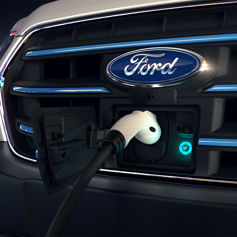Nahaufnahme einer Ford E-Transit Ladestation und des blauen ovalen Ford-Schriftzugs auf dem Kühlergrill. 