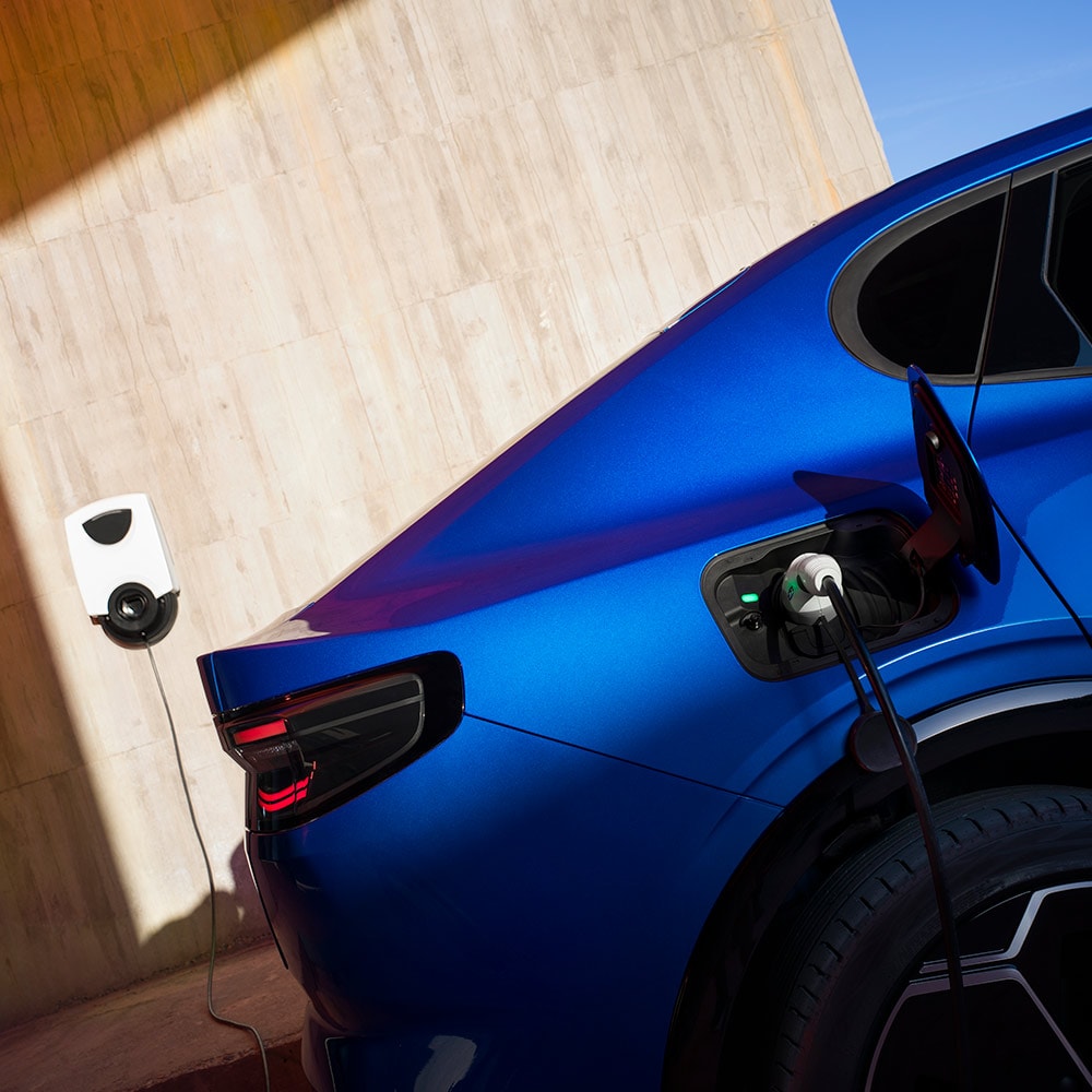 Heckansicht eines blauen Ford Capri Elektrofahrzeugs, das an eine EV-Ladestation angeschlossen ist. 