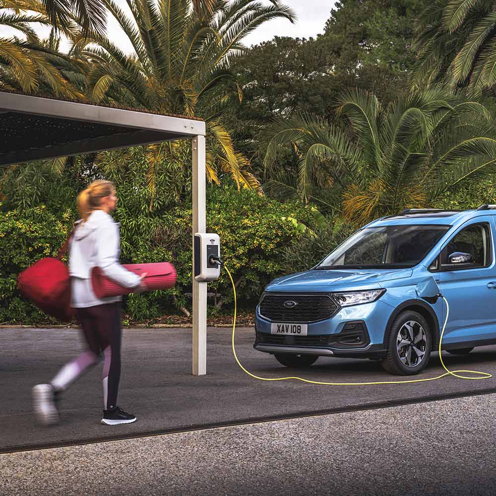 Eine Person mit einer Yogamatte geht auf einen Ford Tourneo Connect Plug-in-Hybrid zu.