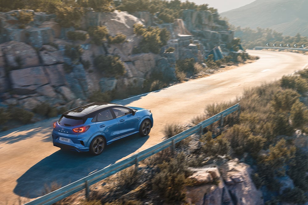 Ein blauer Puma Gen-E fährt eine kurvenreiche Bergstraße entlang.