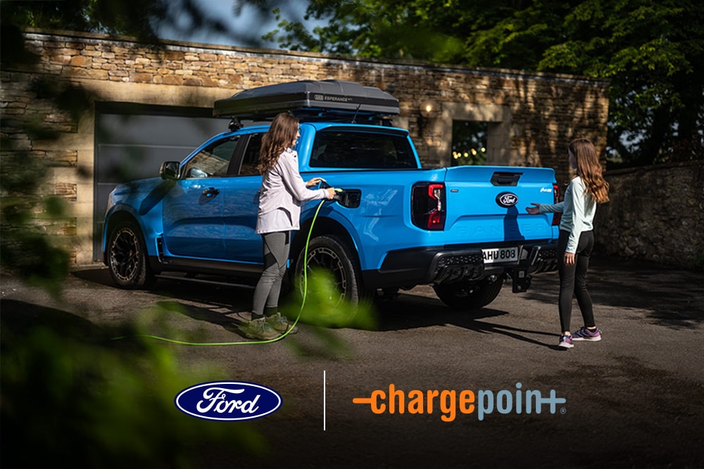 Zwei Personen laden einen blauen Ford Pick-up an einer Garage. Die Logos von Ford und Chargepoint sind sichtbar. 