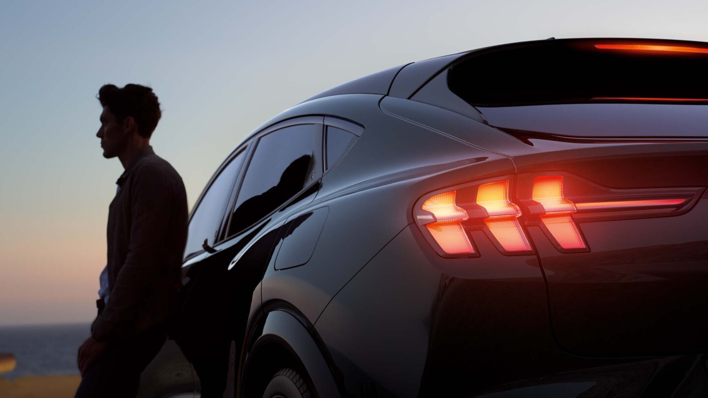 Mann lehnt an einem Mustang Mach-E Mann lehnt an einem Mustang Mach-E