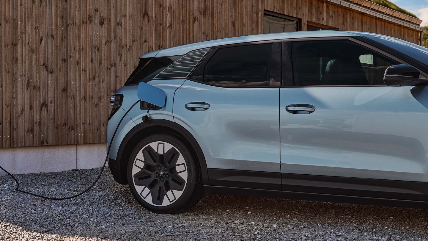 Der neue vollelektrische Ford Explorer in seitlicher Heckansicht an einer Ladestation parkend