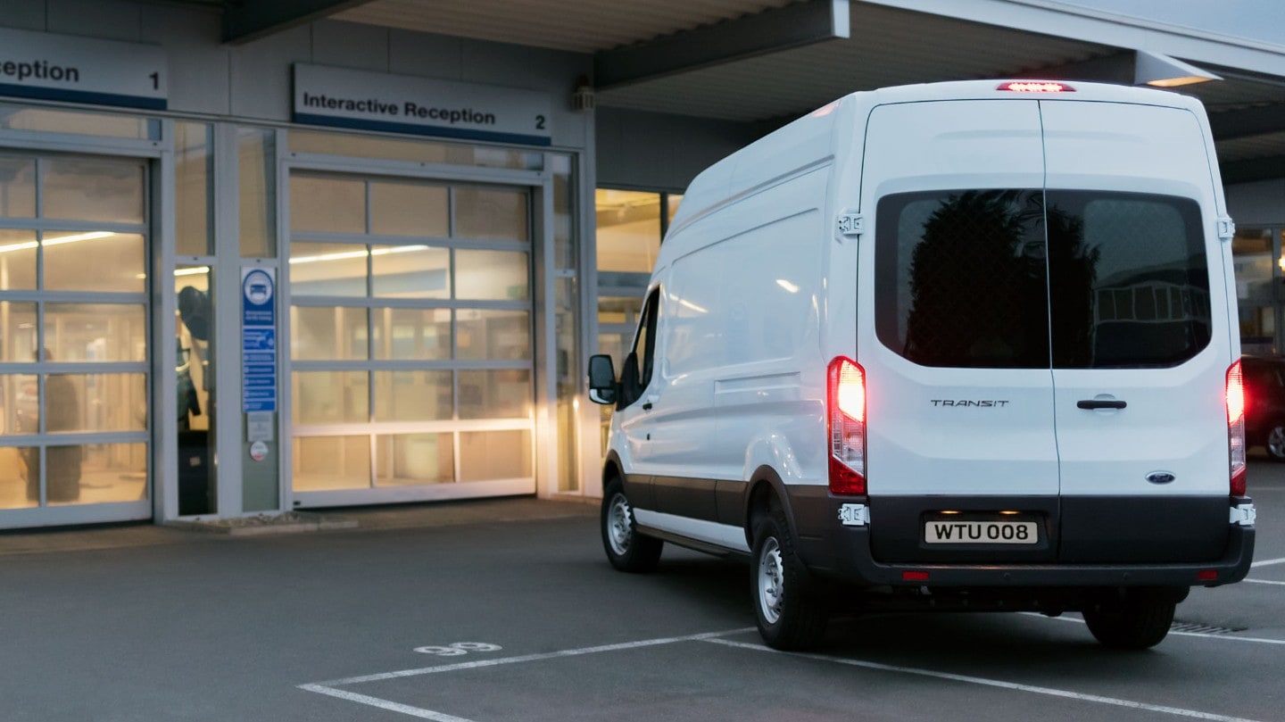 Ford Transit in Weiß in der ¾ Heckansicht parkt vor Ford Werkstatt